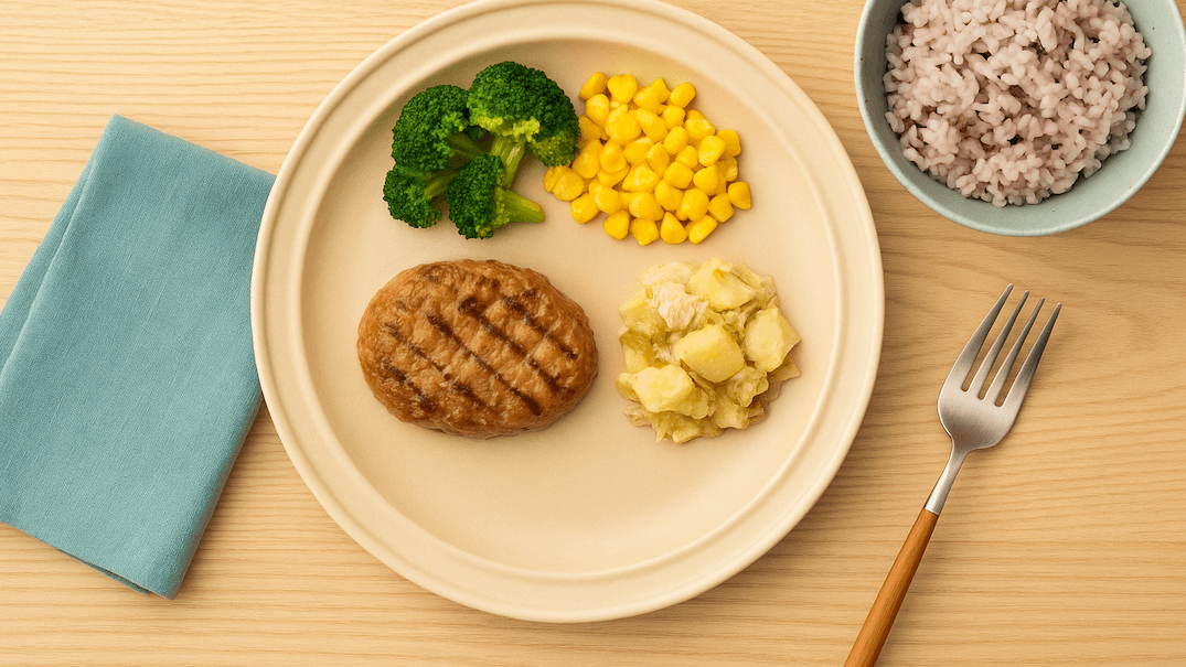 ハンバーグと野菜が盛り付けられた冷凍弁当風のワンプレートと雑穀米の食事