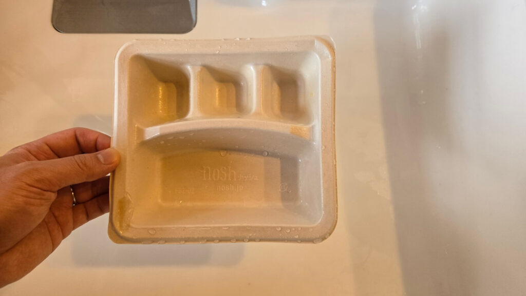 ナッシュの食事用トレーを水洗いしている様子。リサイクルしやすいエコ容器が特徴。

