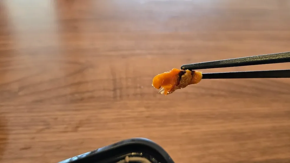 副菜のにんじんが焦げた所を箸でつまんだアップ—ワタミ宅食チキン南蛮セットの彩り副菜をクローズアップ