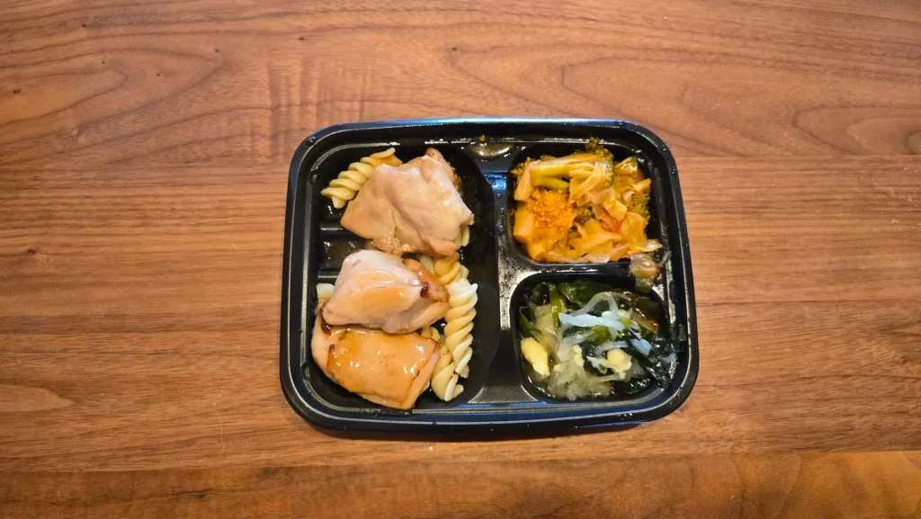 開封したワタミの「直火で焼いた照り焼きチキン」弁当、チキンと副菜がトレーに配置されている