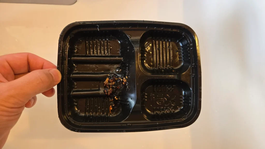 食べ終わって軽く水洗いした後の弁当トレー。焦げたタレとごまが一部に残っている。