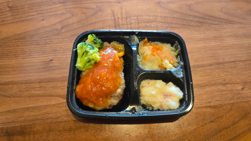 ワタミ宅食ダイレクト「粗挽きハンバーグのトマトソース」の冷凍弁当を加熱後、真上から撮影した画像。主菜・副菜3品入り。