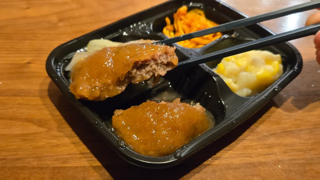 オニオンソースがかかったハンバーグを箸で割った断面のアップ。肉汁のジューシーさが分かる。