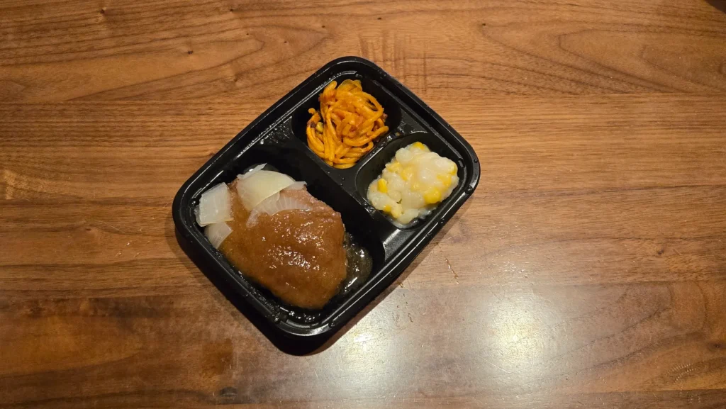 ワタミの宅食ダイレクト「オニオンソースの和風ハンバーグ」弁当を斜め上から撮影。ハンバーグ、スパゲッティ、コーンポテト。